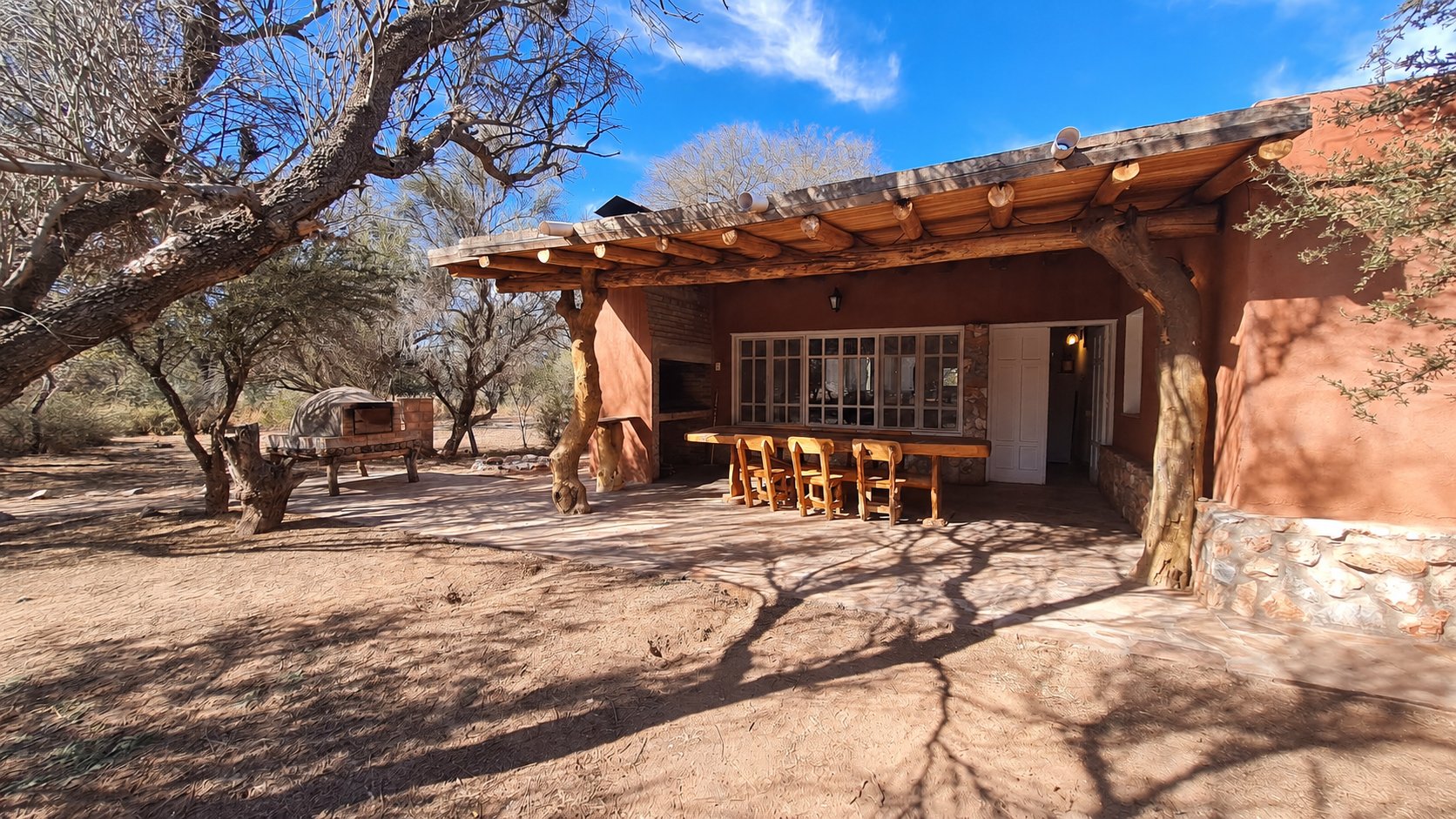 Exterior de Cabañas Ischigualasto con galería de madera y árboles del entorno de campo
